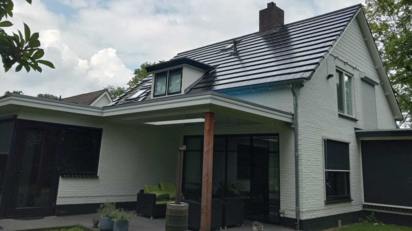 Een vrijstaand wit huis met een nieuw dak van donkere pannen, gezien vanuit de tuin