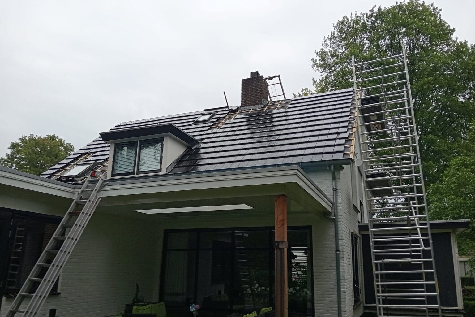 Achterzijde van een witte woning met dakkapel en een steiger tegen het vernieuwde dak