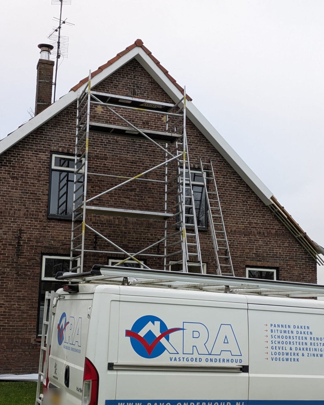 Bakstenen kopgevel in de steigers voor gevelrenovatie, met de werkbus ervoor