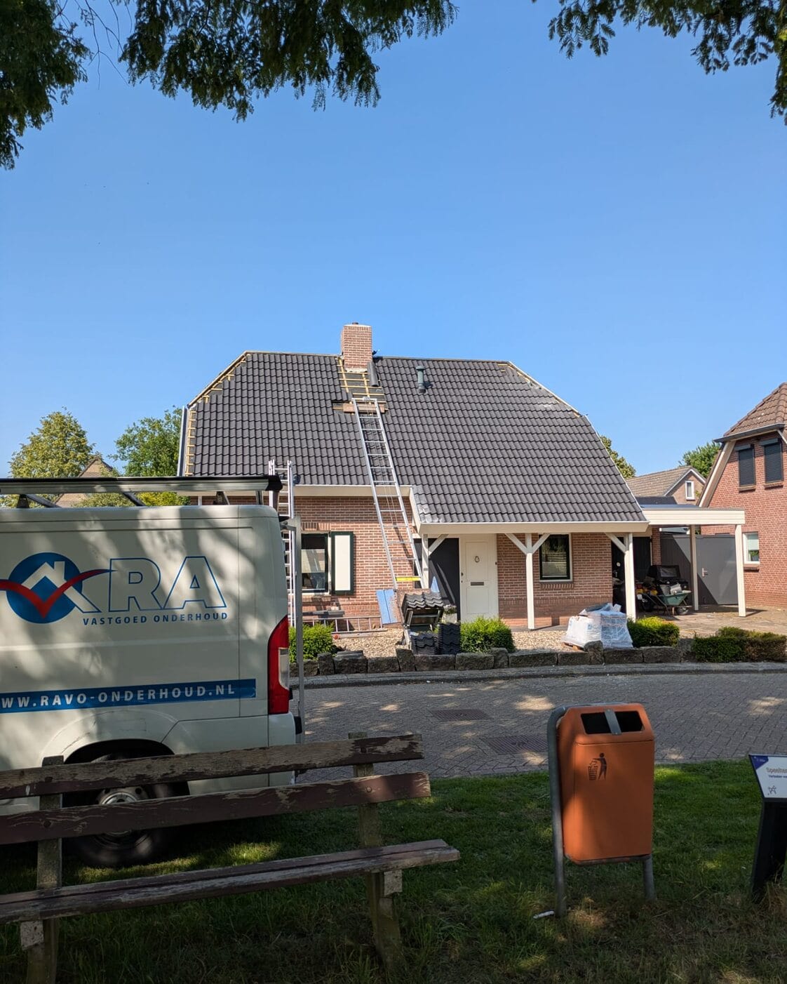 Ladder op een pannendak naar de schoorsteen, met de werkbus op de oprit